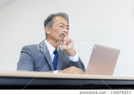 Senior businessman thinking while looking at a computer Senior businessman thinking while looking at a computer 130876813
