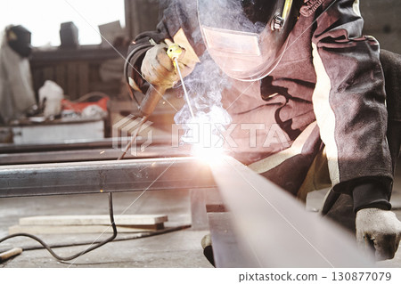 Worker in safety mask welds metal at industrial enterprises. 130877079