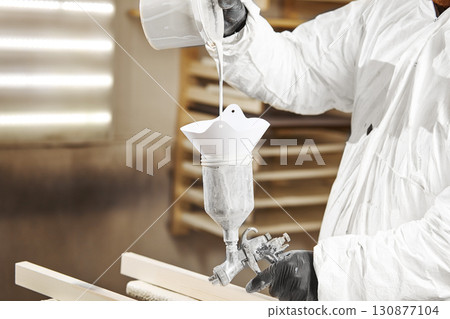 Man pours paint into the sprayer before painting the wood. 130877104