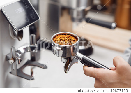 Barista Holding a Perfectly Filled Portafilter in Front of Professional Coffee Grinder 130877133