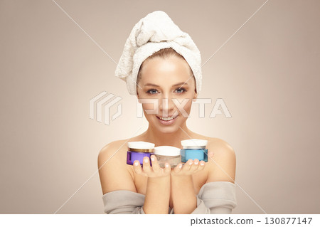 Happy woman with clean fresh skin hold a different of face care creams, wearing in bathrobe and towel on head. Cosmetology, beauty and spa. Concept of skin rejuvenation without surgery. 130877147