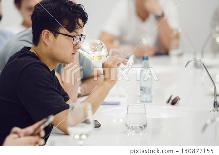 Asian ethnicity sommelier tasting white wine based smelling during study in wine school. Alcoholic beverages degustation. Professional occupation. Asian ethnicity sommelier tasting white wine based smelling during study in wine school. Alcoholic beverages degustation. Professional occupation. 130877155
