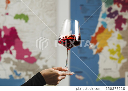 Elegantly Held Red Wine Glass by Faceless Figure Against Map Background Elegantly Held Red Wine Glass by Faceless Figure Against Map Background 130877218