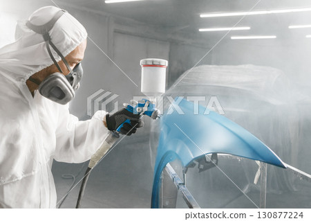 Car repair painter in protective overalls and painting a respirator car wing in the paint chamber 130877224