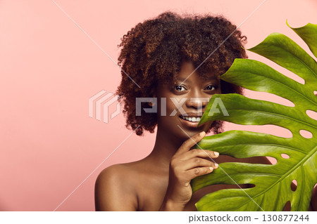 Afro-american girl peeks out from behind monstera leaf. Afro-american girl peeks out from behind monstera leaf. 130877244