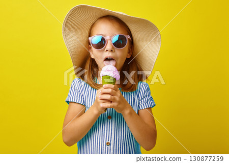 Little girl eating ice cream on isolated yellow background. 130877259