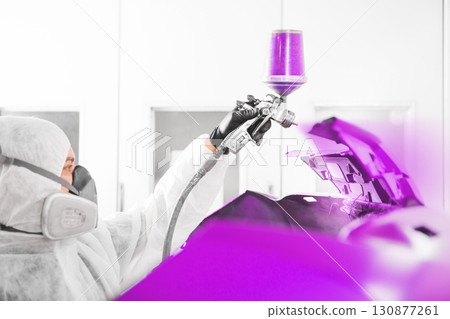 Spray painter worker in protective glove with airbrush pulverizer painting car element in white paint chamber. 130877261