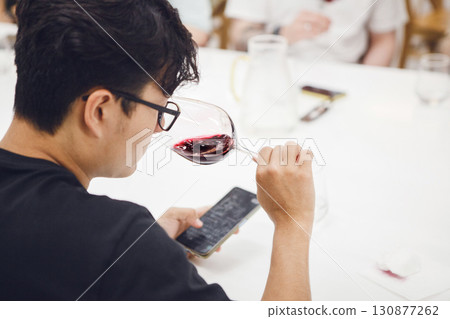Asian ethnicity sommelier wearing in black t-shirt tasting white wine during wine experts lecture or training. Wine experts association, sommelier school, professional development. 130877262