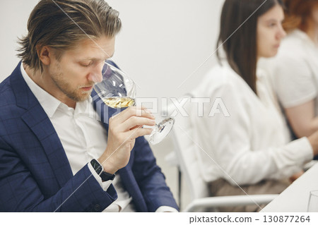 Good looking caucasian ethnicity man tasting white wine from glass being trained as sommelier at school of bartenders and waiters. 130877264