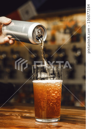 Pouring Cold Beer From an Aluminum Can Into Glass With Rich Foam at Bar Counter Pouring Cold Beer From an Aluminum Can Into Glass With Rich Foam at Bar Counter 130877284