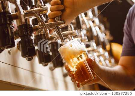Bartender Pours Fresh Beer From Tap Into Glass at Vibrant Bar Counter in Evening Bartender Pours Fresh Beer From Tap Into Glass at Vibrant Bar Counter in Evening 130877290