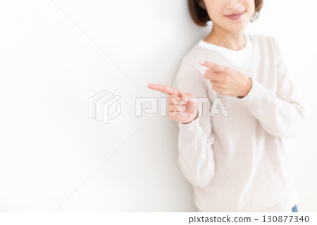 一位穿著休閒服的中年婦女指著一處白牆空間 一位穿著休閒服的中年婦女指著一處白牆空間 130877340