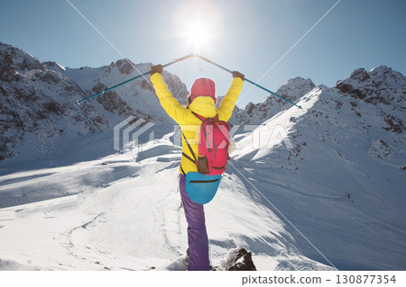 Happy Woman Raised UP Hands Holding Trekking Poles Looking To the Sun Standing with Back of Camera 130877354