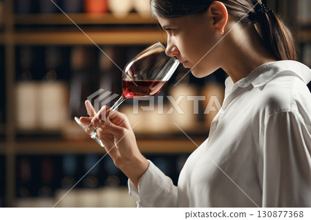 Close up profile portrait of professional woman sommelier in wine cellar degustation red wine in glass, smelling and analyzing.  130877368