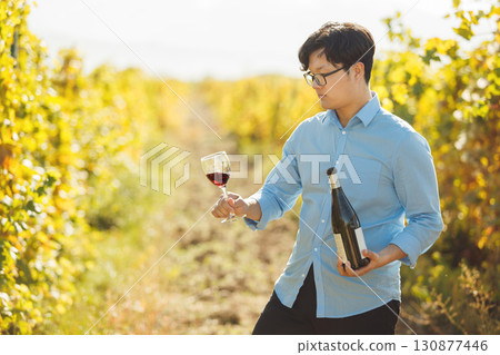 Asian Sommelier Tasting Red Wine in Sunlit Vineyard 130877446