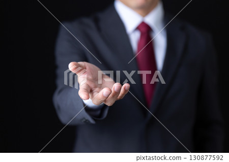A middle-aged male businessman in a suit holding one hand out in front of him A middle-aged male businessman in a suit holding one hand out in front of him 130877592