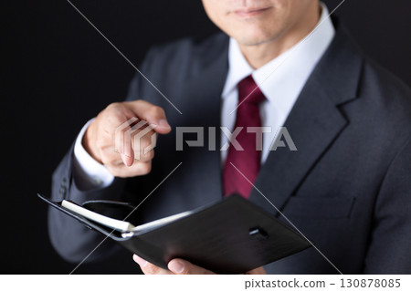 A middle-aged male businessman in a suit checking his notebook A middle-aged male businessman in a suit checking his notebook 130878085