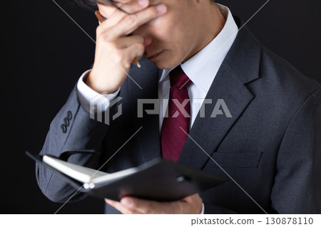 A middle-aged male businessman in a suit who is depressed after looking at his notebook A middle-aged male businessman in a suit who is depressed after looking at his notebook 130878110