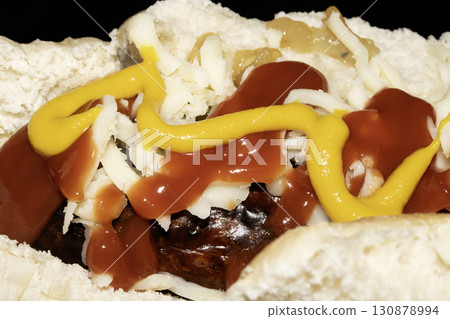 Close up of mustard and ketchup tomato sauce on a hot dog and cheese roll Close up of mustard and ketchup tomato sauce on a hot dog and cheese roll 130878994