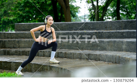 Fitness enthusiast doing leg stretches on stone steps during outdoor training session 130879204