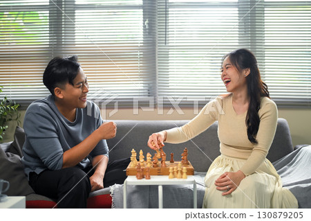 Happy young couple enjoying leisure time playing chess together at home. 130879205