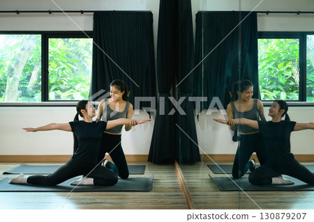 Female trainer helping woman practice yoga stretch on mat in a bright studio 130879207