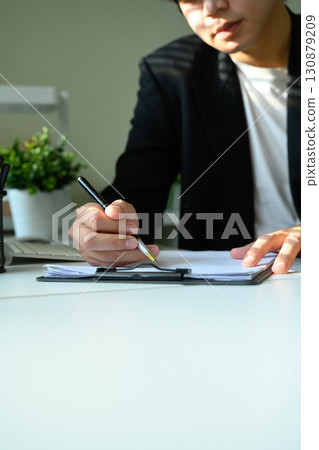 Hands of businessman signing documents on clipboard in office Hands of businessman signing documents on clipboard in office 130879209