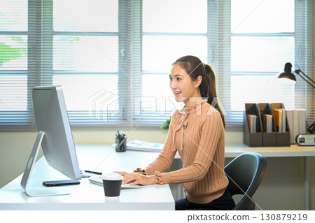 Smiling businesswoman working in modern office with natural light 130879219