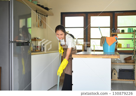 Smiling young woman doing household chores, mopping modern kitchen floor Smiling young woman doing household chores, mopping modern kitchen floor 130879226