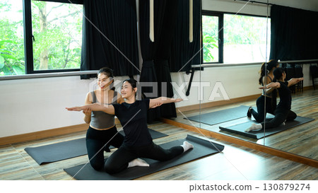 Smiling young woman practices yoga with the guidance of her instructor in a fitness studio Smiling young woman practices yoga with the guidance of her instructor in a fitness studio 130879274