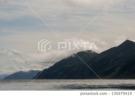 Steep coastal mountainside with drifting mist above ocean Steep coastal mountainside with drifting mist above ocean 130879419