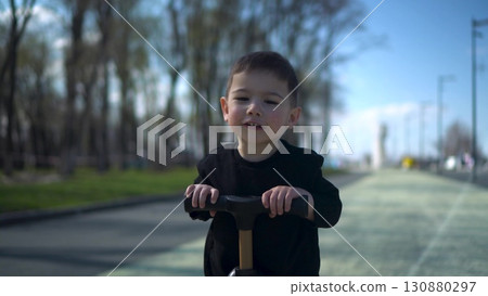 A Joyful Young Child Happily Riding a Colorful Scooter in the Park, Embracing Fun and Adventure 130880297