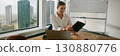 A businesswoman is diligently reviewing important documents within a modern office environment 130880776