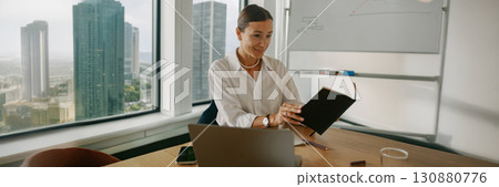 A businesswoman is diligently reviewing important documents within a modern office environment 130880776