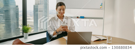 A professional woman is actively engaged with her mobile device while in the office environment 130880834