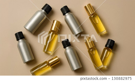 Assorted metallic and glass bottles filled with golden liquid arranged artistically on a soft beige background, showcasing beauty and wellness product packaging design concepts 130882975
