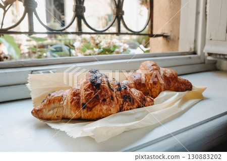 two croissants on parchment paper by a windowsill 130883202