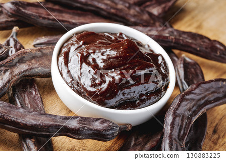 carob cream in a bowl among pods on a wooden table 130883225