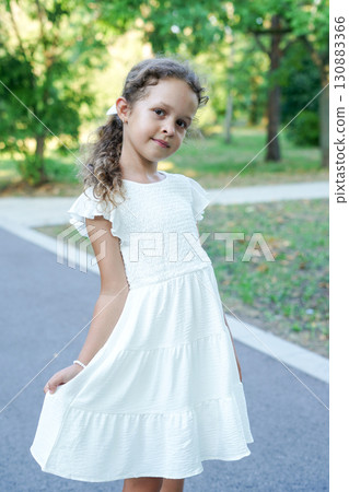 child girl poses gracefully outdoors in a flowing white dress 130883366