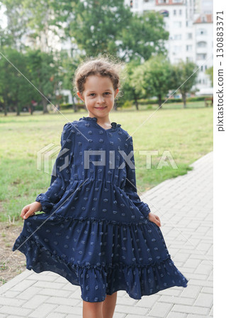 A smiling young girl poses outdoors in a navy blue long-sleeved dress 130883371