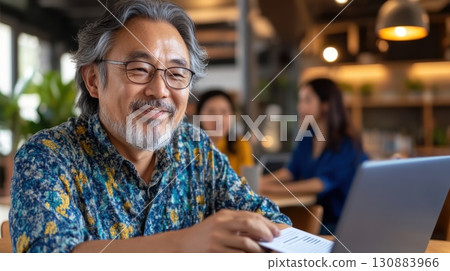 Middle-aged Asian man reviewing feedback form on laptop during corporate workshop in modern, daylight-filled setting. Survey research answer checklist 130883966