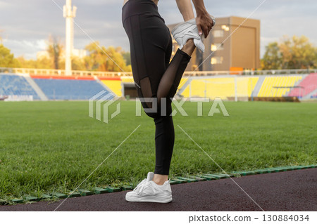 A woman in athletic wear is performing a quadriceps stretch on a running track A woman in athletic wear is performing a quadriceps stretch on a running track 130884034