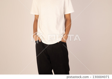 Man is standing with their hands in their pockets, wearing a white t-shirt  130884071