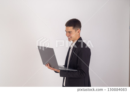 The man in the suit is holding a laptop and looking at its screen. 130884083