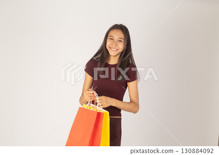 A young woman with long hair is smiling and holding two colorful shopping bags 130884092