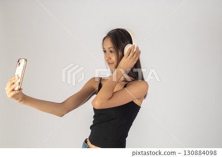 The model is taking a selfie with a smartphone while wearing headphones 130884098
