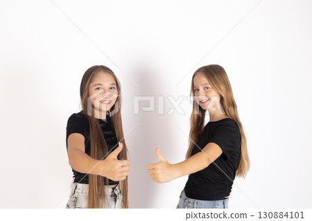 Two young girls are smiling and giving a thumbs-up gesture towards the viewer. 130884101