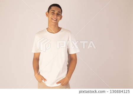 man in a white t-shirt and beidge pants stands with his hands in his pockets  130884125