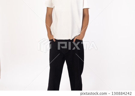 Man wearing a white t-shirt and black pants is standing with hands in their pock Man wearing a white t-shirt and black pants is standing with hands in their pock 130884242