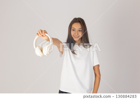 Woman is holding out a pair of white headphones towards the viewer while smiling 130884283